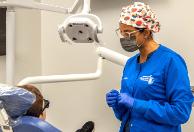A woman in blue coat and surgical mask standing next to a patient, representing common dental issues in children