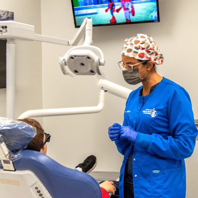A woman in blue coat and surgical mask standing next to a patient, representing common dental issues in children