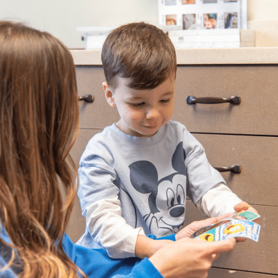 A little boy holding a card, while a member of the dental team talks to him, representing thumb sucking and dental development
